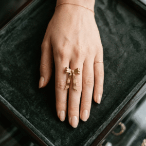 A beautiful manicured hand of a female model styling a textured gold plated ribbon bow ring on her finger.
