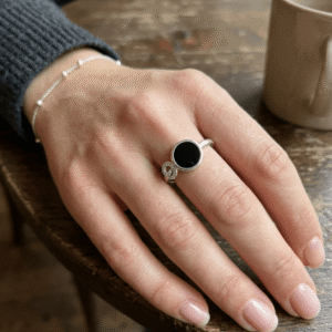 A beautiful manicured hand of a female model styling a silver plated black stone halo ring with a crystal paved twisted band on her finger.