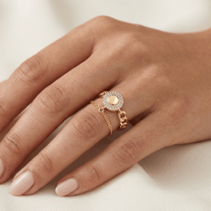 A beautiful manicured hand of a female model styling a gold plated chain link ring with a rhinestone open circle charm on her finger.