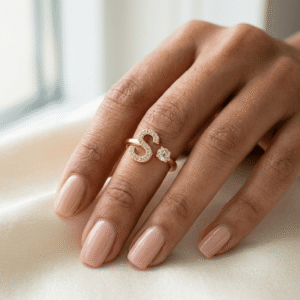 A beautiful manicured hand of a female model styling an adjustable gold initial letter 'S' bypass ring with a crystal solitaire.