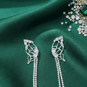 Silver Butterfly Rhinestone Tassel Drop Earrings against a green satin background with Gems & Jewels branding.