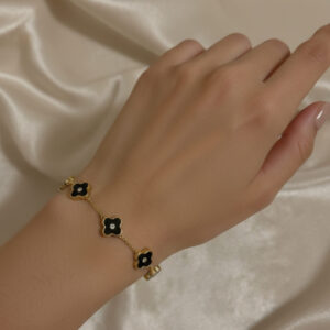Dainty 18k gold plated station chain bracelet featuring multi-motif black enamel four-leaf lucky clover charms on a woman's wrist.
