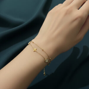 A premium gold double strand clover bracelet with white flower motifs and star charms displayed on a woman's wrist against a deep teal background.