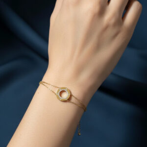 A premium gold crystal circle bracelet featuring a double chain and pave zirconia stone ring displayed on a woman's wrist against a deep blue background.