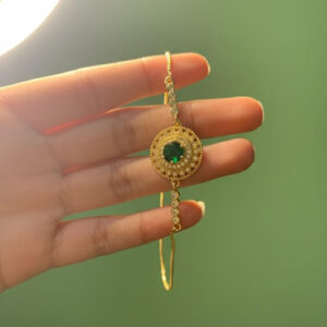A premium gold green crystal bracelet with a circular emerald-style center stone held up by a person's fingers against a green background.