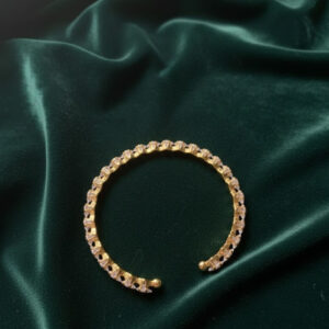 A premium gold crystal cuff bangle with an open eternity design displayed on a rich dark green velvet cloth background.