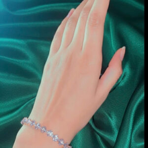 A premium gold crystal tennis bracelet with a continuous strand of shining gems displayed on a woman's wrist against a green silk background.