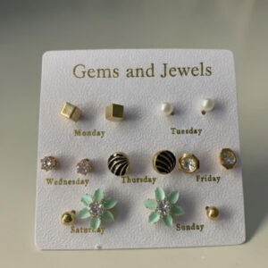 A premium gold stud earrings set featuring seven pairs of weekly daily studs labeled Monday to Sunday on a white card.