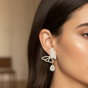 A model wearing premium gold crystal butterfly earrings with a pave wing design and dangling tear-drop gems.