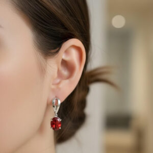 A model wearing premium silver red stone earrings with an oval-cut red crystal gemstone drop against a soft blurred background.