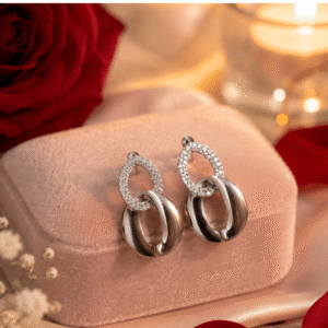 Luna Sparkle Drop Earrings with crystal-studded silver oval links displayed on a blush pink velvet jewelry box with roses and candlelight.
